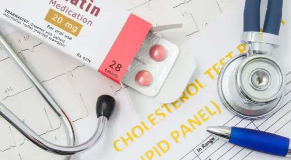 Lekarz bada wyniki cholesterolu, obok leży stetoskop i opakowanie leku Statin 20 mg.