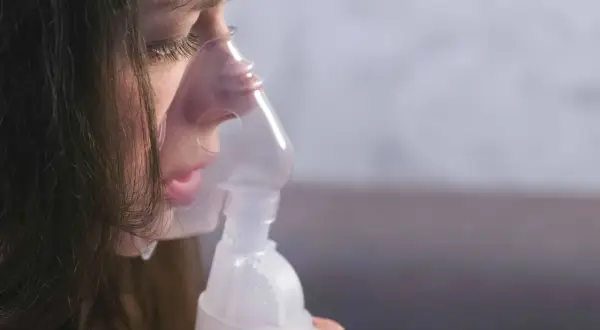 Dziewczynka z maską inhalatora na twarzy, która pomaga jej w walce z anoro.