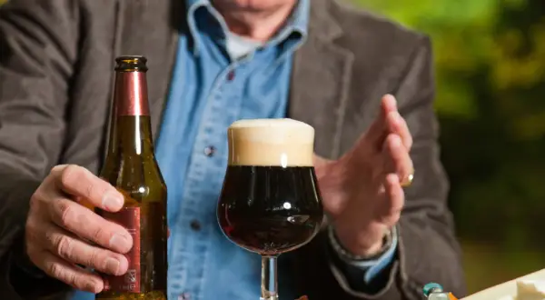 Mężczyzna trzyma butelkę piwa obok pełnego kufla. Czy po szczepieniu można pić alkohol? To pytanie nurtuje wielu.