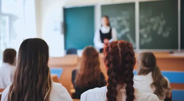Uczniowie słuchają lekcji o edukacji zdrowotnej. Nauczycielka stoi przed tablicą, a dzieci siedzą w ławkach, skupione na przekazywanej wiedzy.