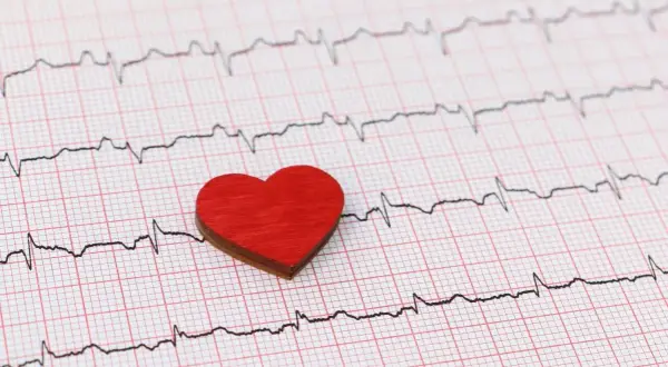 Czerwone serce na tle zapisu EKG. Zwróć uwagę na subtelne zmiany, które mogą sygnalizować cichy zawał objawy.
