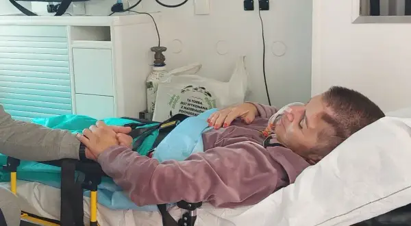 Pacjentka po pęknięciu tętniaka mózgu, z maską tlenową, trzymająca się bliskiej osoby. Rokowania niepewne.