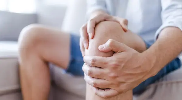 Mężczyzna trzyma się za bolące kolano, sugerując uraz kolana, który może być klasyfikowany według ICD 10.