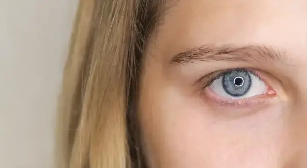 Jasne, niebieskie oko z wąskimi źrenicami, otoczone blond włosami.