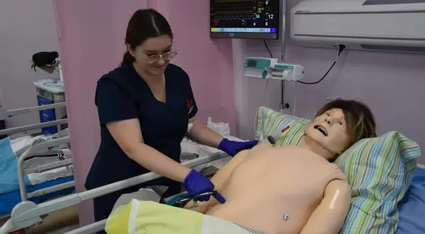 Studentka medycyny ćwiczy procedury medyczne na fantomie. Monitor pokazuje parametry życiowe.