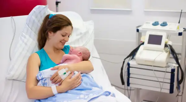 Szczęśliwa mama tuli noworodka po cesarce francuskiej. W tle sprzęt medyczny.