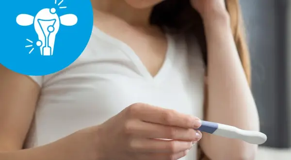 Kobieta trzyma test ciążowy, a obok widnieje symbol probella z zaznaczonymi problemami z płodnością.