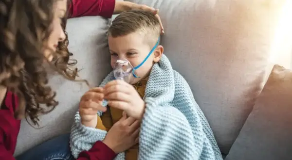 Chłopiec z maseczką nebulizatora, otulony kocem, czuje się jakby dopadła go klątwa Ondyny. Mama czule go głaszcze.
