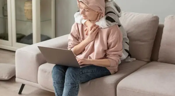 Kobieta z dzieckiem na kolanach pracuje przy laptopie. Dziecko ją przytula, szukając wsparcia, jak u psychoonkologa.