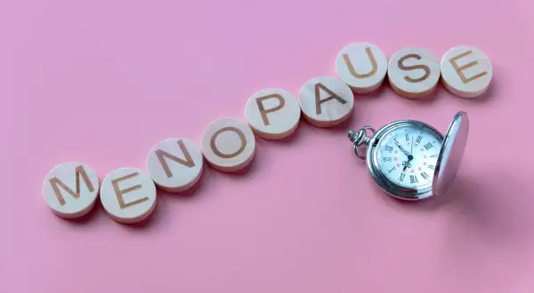 Drewniane kółka z literami układają napis "MENOPAUSE" obok kieszonkowego zegarka. Pytanie "ile trwa menopauza forum" nasuwa się samo.