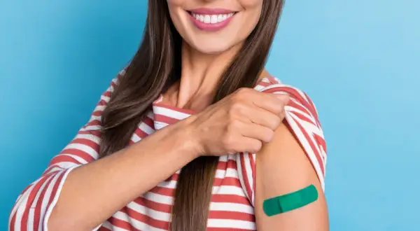 Uśmiechnięta kobieta z zielonym plastrem na ramieniu po szczepieniach HPV dla dorosłych. Dba o zdrowie.