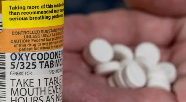Oxycodone co to za lek? Na zdjęciu widać butelkę z lekiem i garść białych tabletek.