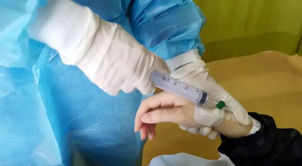 Ręka pacjenta z wenflonem, pielęgniarka w rękawiczkach podaje lek, prawdopodobnie hydroxycarbamid.