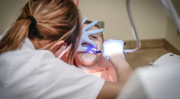 Dentysta z niebieskim światłem bada zęby dziecka.