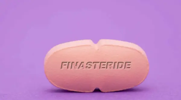 Różowa tabletka z napisem FINASTERIDE na fioletowym tle.