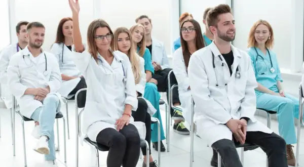 Grupa studentów medycyny na wykładzie. Jedna z nich podnosi rękę, zadając pytanie. Może to być początek jej drogi do zostania rejestratorką medyczną, kurs za darmo.