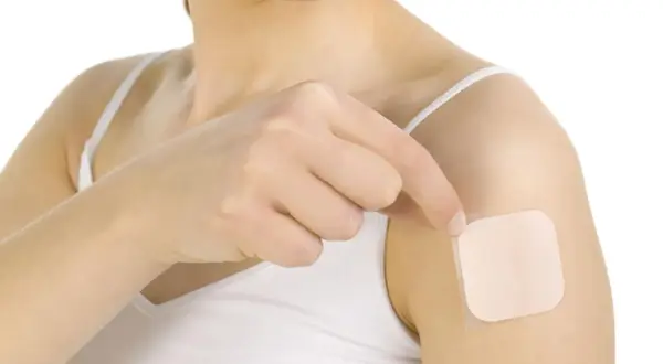 Kobieta aplikuje na ramię plaster przeciwbólowy na receptę, szukając ulgi w bólu.