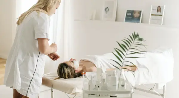 Dermatolog wykonuje zabieg na twarzy pacjentki leżącej na kozetce w gabinecie.