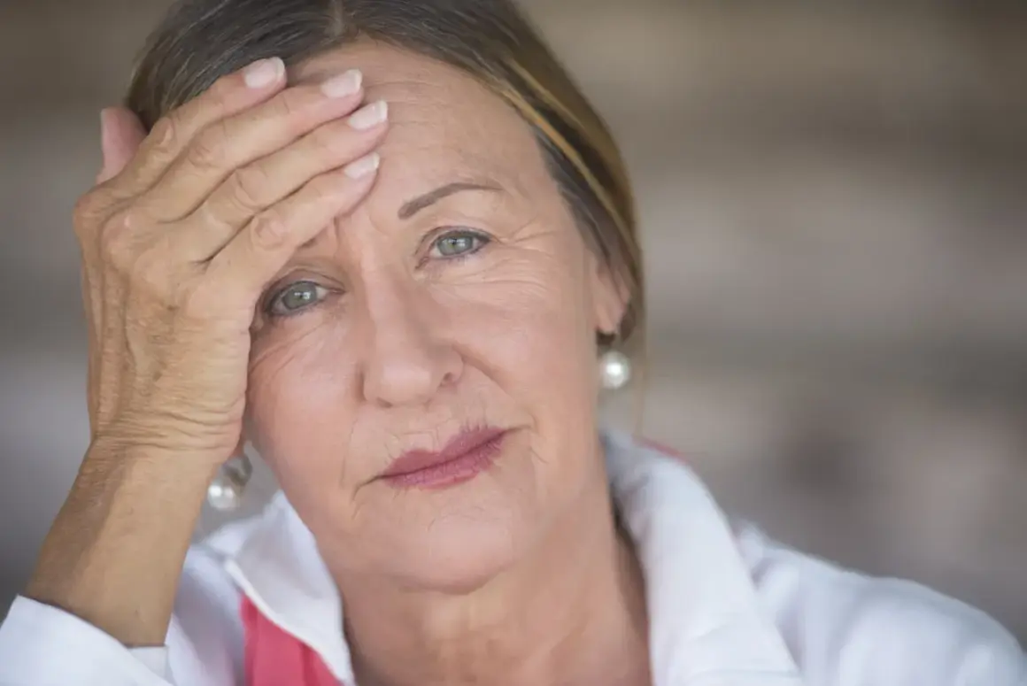 Zmęczona kobieta z ręką na czole, być może rozważa hormonalną terapię zastępczą.