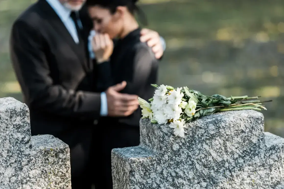 Para wspiera się na cmentarzu, obok wiązanki białych kwiatów. Czas na urlop macierzyński po poronieniu, by przeżyć żałobę.