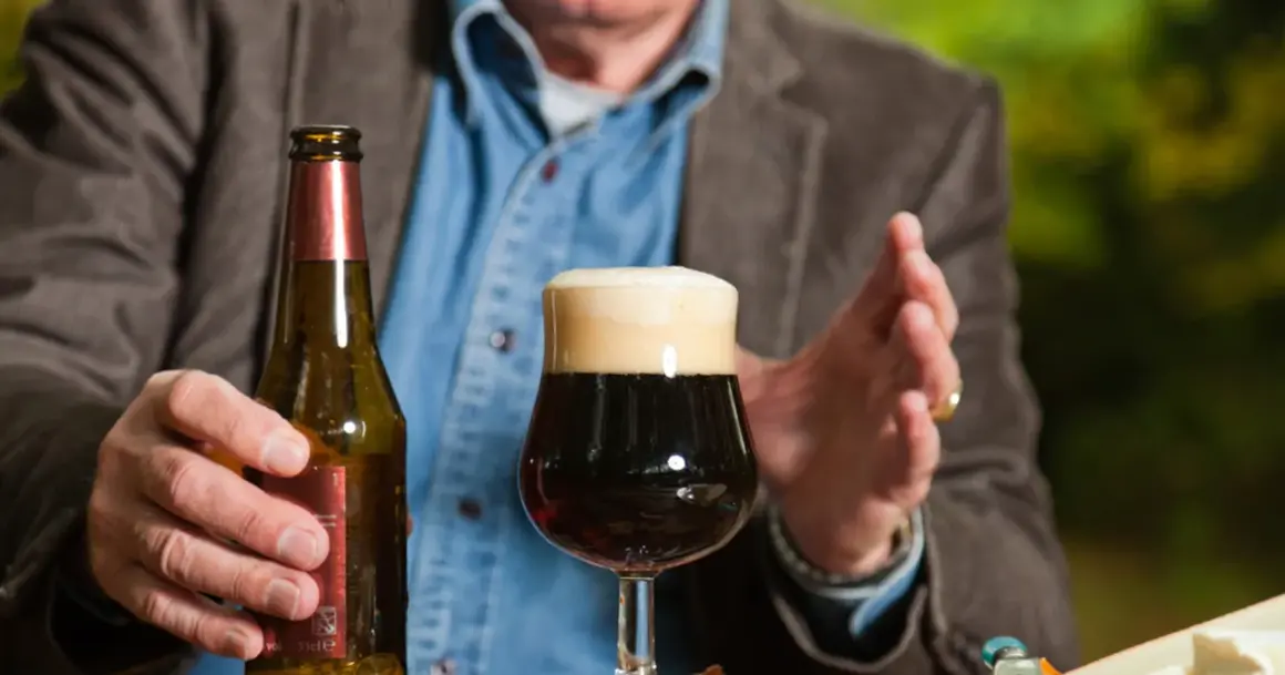 Mężczyzna trzyma butelkę piwa obok pełnego kufla. Czy po szczepieniu można pić alkohol? To pytanie nurtuje wielu.
