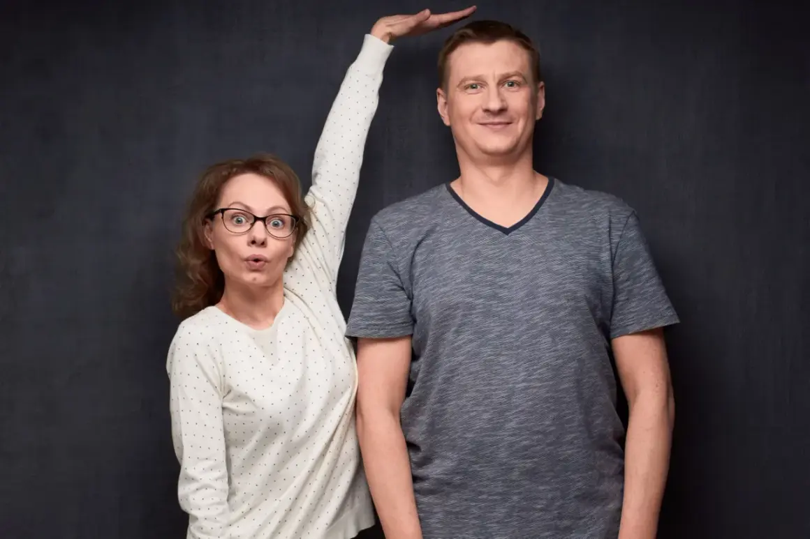 Kobieta z wyrazem zaskoczenia na twarzy próbuje zmierzyć wzrost mężczyzny, który wydaje się mieć gigantyzm.