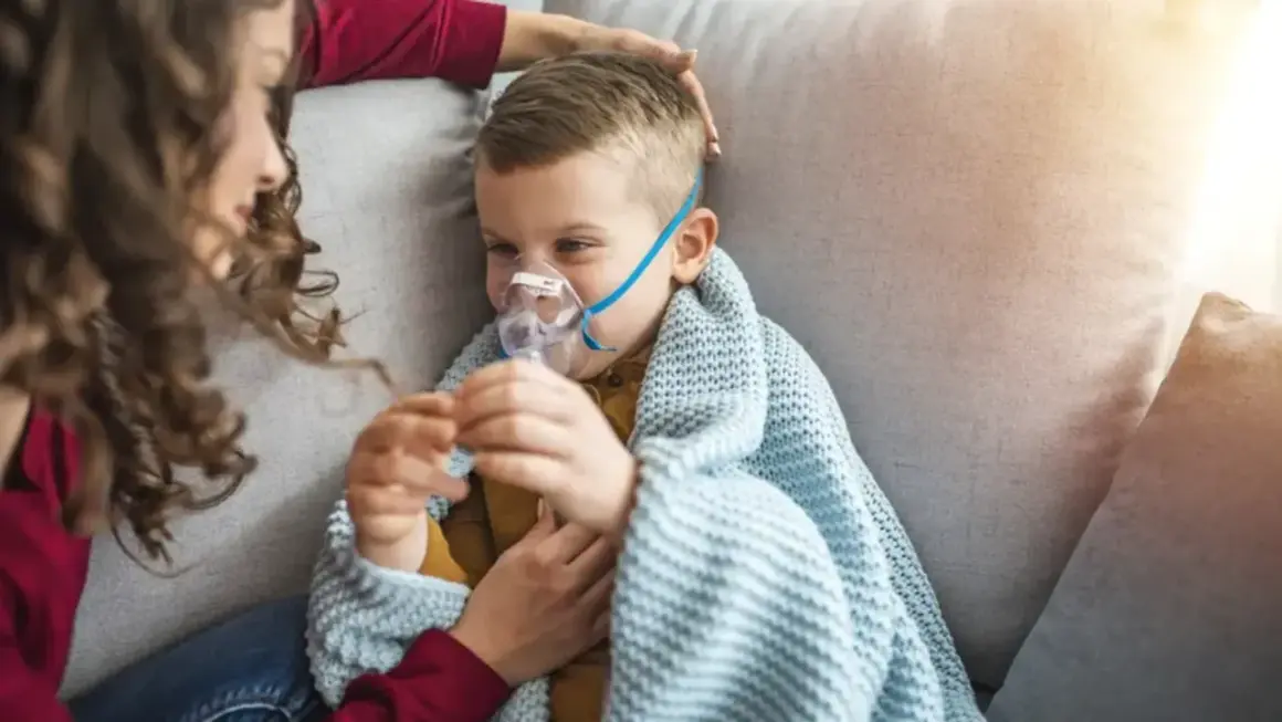 Chłopiec z maseczką nebulizatora, otulony kocem, czuje się jakby dopadła go klątwa Ondyny. Mama czule go głaszcze.