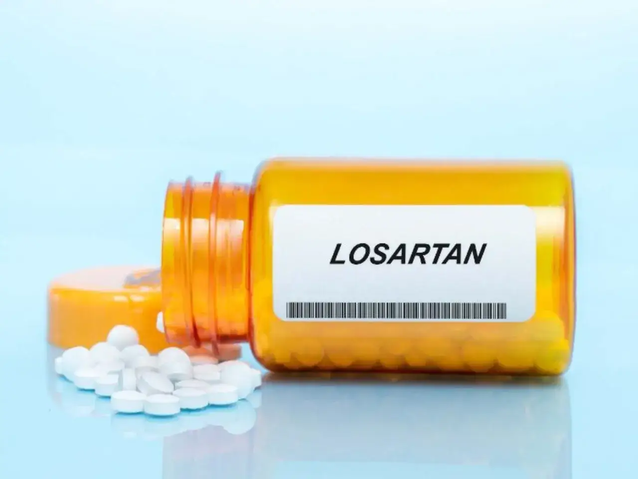 Pomarańczowa butelka z tabletkami Losartan, kilka białych tabletek rozsypanych obok.