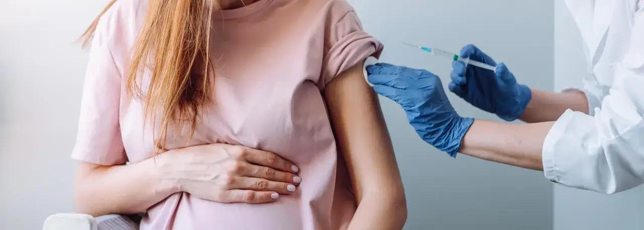 Szczepienie RSV w ciąży chroni mamę i dziecko. Lekarz podaje szczepionkę w ramię przyszłej matki.