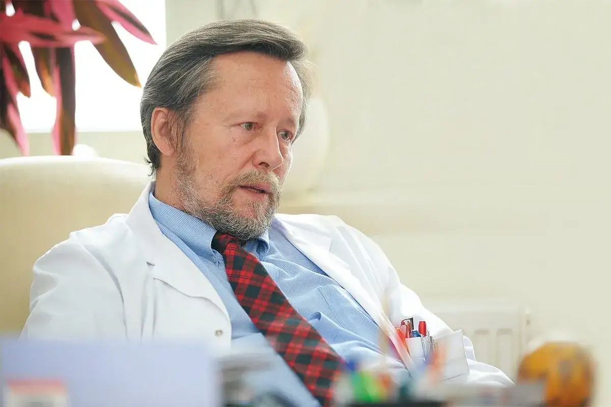 Lekarz w białym kitlu i krawacie w kratę, z brodą, opowiada o nadziei na remisję.