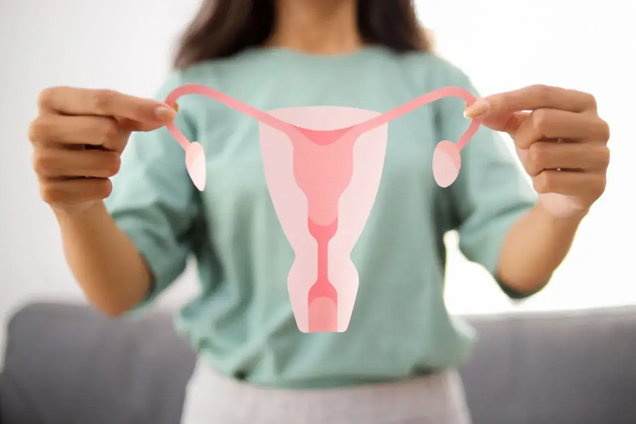 Kobieta trzyma wycięty z papieru model narządów rodnych, symbolizujący temat pcos co to.