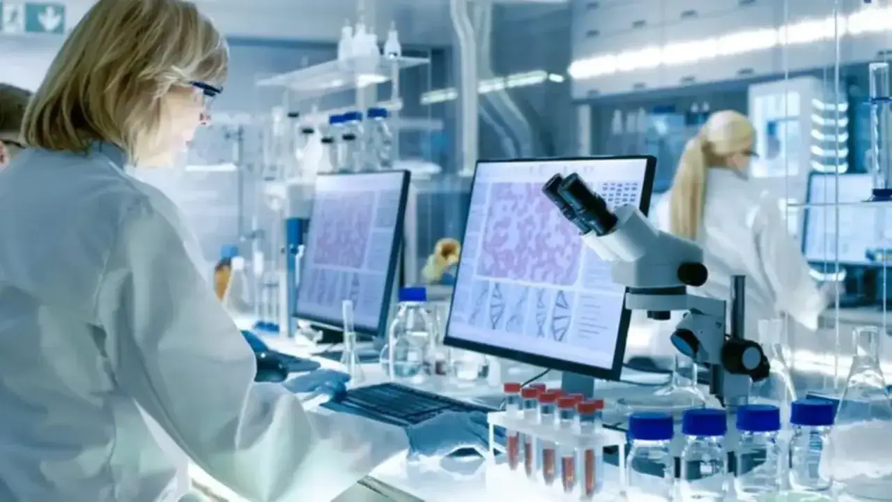 Naukowcy w laboratorium analizują próbki pod mikroskopem i na monitorach, badając co po analityce medycznej.