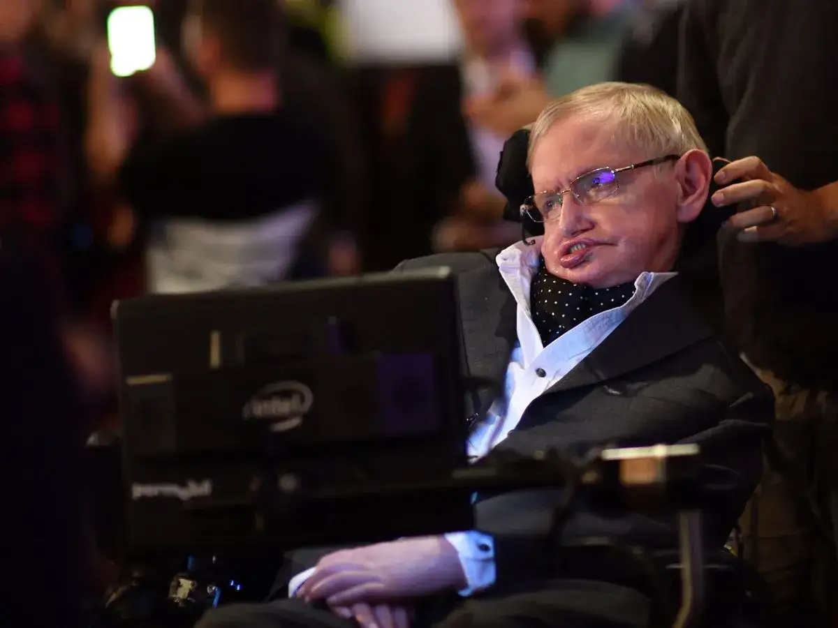 Stephen Hawking w wózku inwalidzkim, z charakterystycznym uśmiechem, mimo swojej choroby.
