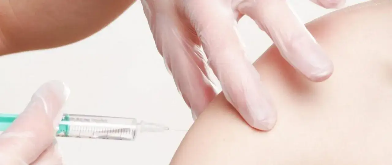 Ręka w rękawiczce podaje zastrzyk, chroniąc przed chorobą polio.