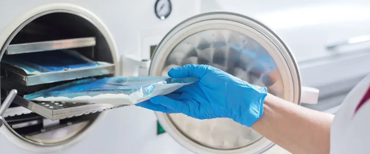 Ręka w niebieskiej rękawiczce wyjmuje pakiet z autoklawu. Technik sterylizacji medycznej zarobki są kluczowe dla bezpieczeństwa pacjentów.