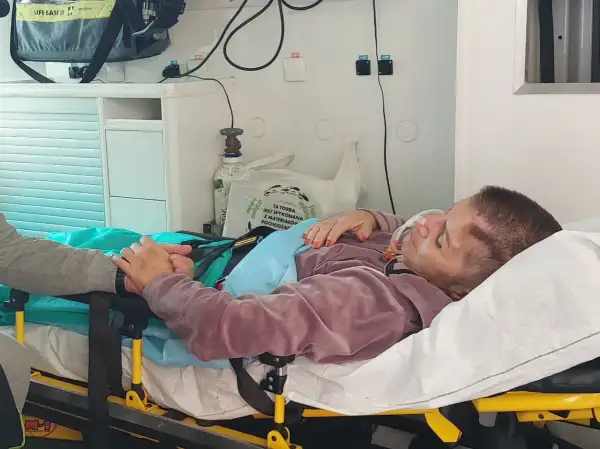 Pacjentka po pęknięciu tętniaka mózgu, z maską tlenową, trzymająca się bliskiej osoby. Rokowania niepewne.